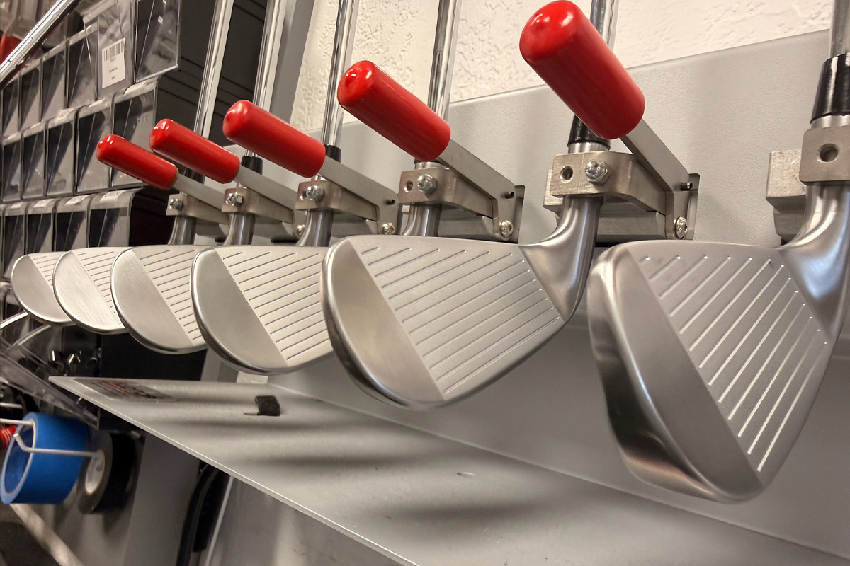 Row of silver metal clamps with red handles attached to a metalworking machine, ready for operation.